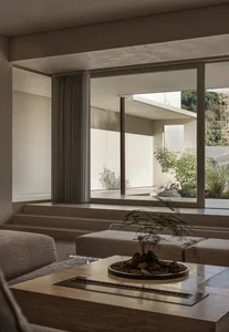 Modern living room with concrete walls and floor, large windows, and a small indoor plant on a table.
