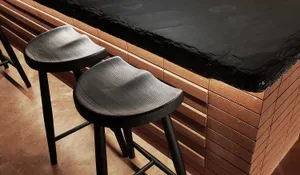 Two minimalist black bar stools with textured seats and wooden legs.