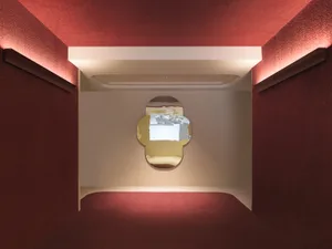 A minimalist interior design with red textured walls, featuring a unique light fixture and a mirror reflective of light and s