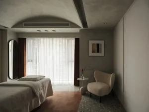 A minimalist bedroom with a bed, chair, and side table, featuring modern materials and a neutral color palette.
