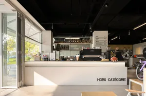 A modern coffee shop interior featuring a white counter with a menu board and a glass door.