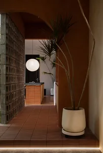 Modern entryway featuring brick walls, concrete arch, potted plants, and a spherical light fixture.