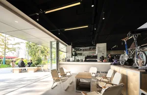 A modern, industrial-style coffee shop interior featuring metal-framed furniture, a concrete counter, and a relaxed seating a