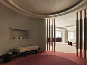 Modern living room with concrete walls, wooden pillars, and red carpet, featuring minimalist furniture and large windows with