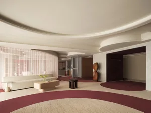 A modern lobby with white sofas, a wooden coffee table, and a textured carpet in shades of red and beige. The ceiling feature