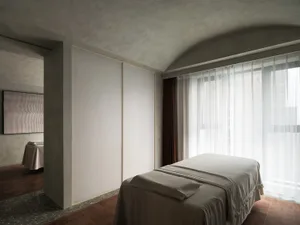 A modern minimalist bedroom featuring neutral tones with a bed, windows, and a striped curtain.