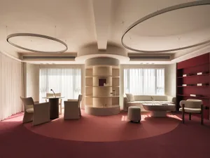 A modern interior space with a circular table, chairs, and bookshelf, featuring neutral-toned furniture and a red carpet.