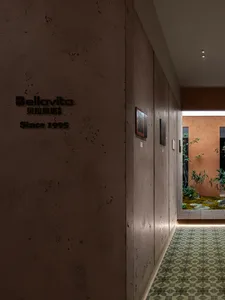 A corridor with concrete walls, artwork, and a view of a garden with a stone pathway and green plants.