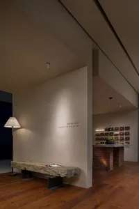 A minimalistic concrete lobby interior with a wooden floor, a stone bench, and a floor lamp.