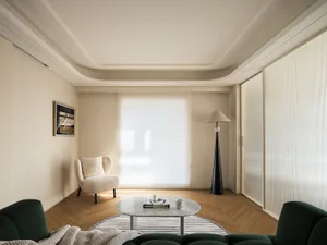 Minimalist living room with wooden furniture and flooring, featuring a white armchair, a green sofa, and a round marble coffe