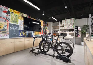 A modern bike shop with metal and wood elements, featuring a large screen TV and several bicycles on stands.