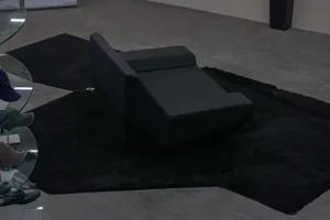 A black leather lounge chair placed on a black rug in a minimalist room setting.