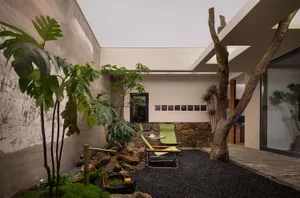 Modern living room with concrete walls, rock landscaping, and green outdoor furniture.