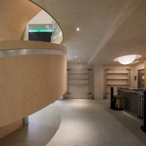 Angle view of a modern office lobby with a curved wooden wall, concrete flooring, and metal shelves.