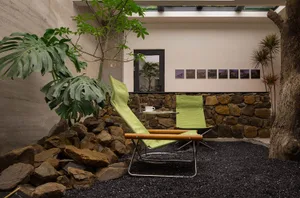 A modern patio with green folding chairs placed on a stone rock garden surrounded by plants and a stone wall.