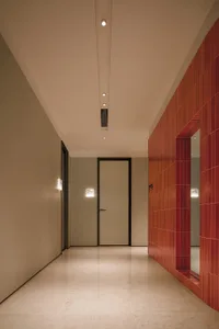 A minimalist corridor featuring tile and marble flooring, with a red-tiled wall on the right and a door at the end.