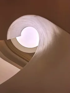 Circular staircase with smooth concrete walls, viewed from the bottom looking up towards the light at the top.