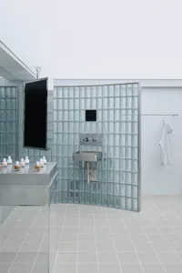 Modern bathroom with glass block tiles, stainless steel sink, and wall-mounted television