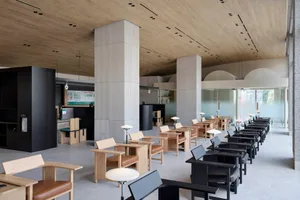 Interior of a modern coffee shop featuring wooden furniture, concrete columns, and large glass windows.