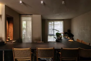 A modern dining room featuring a black rectangular table surrounded by wooden wicker chairs, with a person adjusting the blin