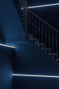 Modern staircase with blue walls, metal railing, and illuminated lines.