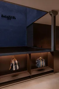 A modern storefront with a black metal wall and two handbags hanging below it.