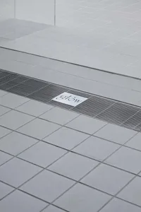 A minimalist bathroom floor with grey tiles and a concrete accent strip.