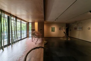 A spacious art gallery with minimalist decor featuring dry tree branches as central elements and a view of the outdoors.