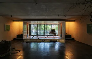 A modern living room with concrete walls and wooden furniture, featuring a minimalist design and large windows.