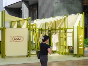 A modern outdoor fashion market booth with yellow-green frames, suspended fabric, and clothing displays.