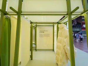 A modern retail display with green wooden columns and a white background featuring a large beige coat.