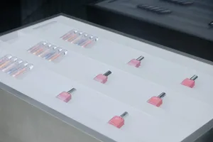 A white, frosted glass display case showcasing a variety of pink-colored bottles and tubes of cosmetics, organized neatly on 