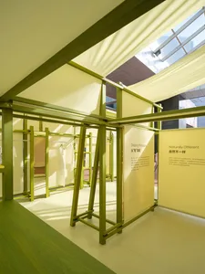 A minimalist showroom with wooden structural beams and yellow fabric partitions.