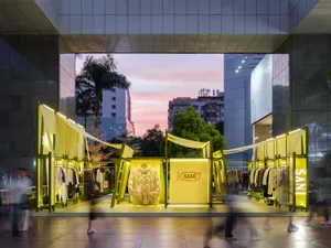 Modern retail storefront illuminated with yellow lighting features a mannequin wearing a white jacket and has a yellow banner