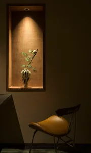 A ceramic vase with a branch and leaves sitting in a small recessed shelf.