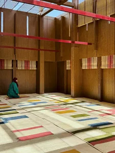 A woman kneeling on a minimalist space with a textile floor and wooden walls.