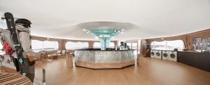 A spacious hotel interior featuring a central bar area with a glass dome ceiling, wooden flooring, and multiple seating optio