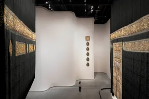 A spacious gallery with large black and gold hanging textiles, a white wall, and a single person standing in the middle.