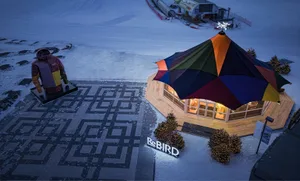 A snow-covered winter tent structure with a multi-colored tent roof and illuminated interior in a snowy environment.