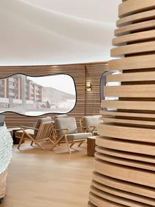 A modern hotel lobby featuring wooden walls and furniture, with a view of snowy mountains through a large window.