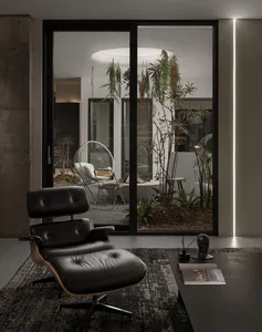 Modern living room with a black metal and leather lounge chair in front of a large window with plants.