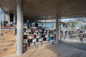 A modern library interior with concrete walls and floors, featuring bookshelves filled with books.
