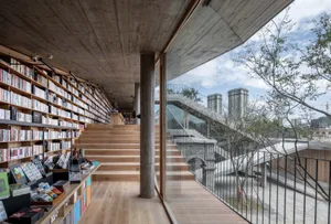 現代圖書館室內，木質書架、混凝土天花板，以及俯瞰城市景觀的玻璃牆。