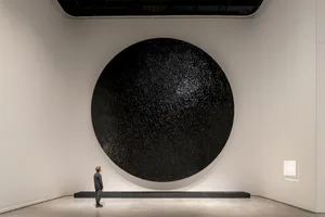 A large, textured black circle hanging on a white wall in a minimalist space.
