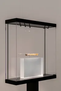 A minimalist glass key case with a single ornate key inside, displayed in a museum setting.