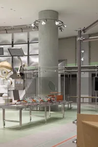 An industrial-style exhibition with metal tables and a large robot in the background.