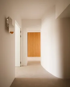 Modern minimalist hallway with concrete walls and floor, leading to a wooden closet.