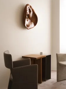 A modern interior design featuring wooden furniture with metal legs and a minimalist wall sculpture.