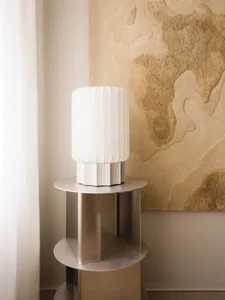 A minimalist, white metal side table with a lampshade on top.
