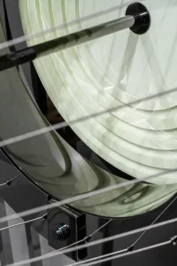Modern abstract metal sculpture on a black pedestal. The piece features a circular, segmented design with a reflective surfac